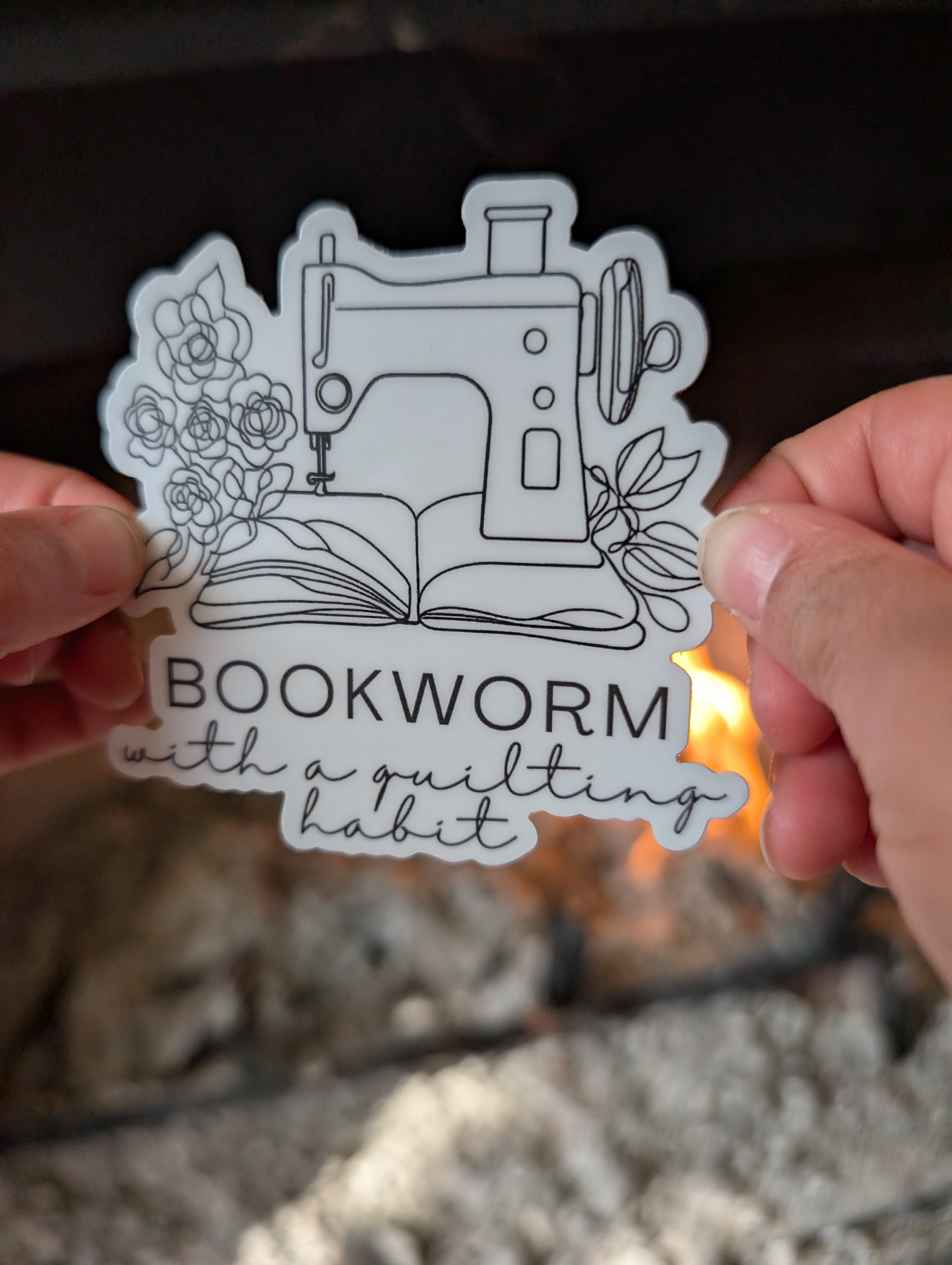 Sticker with sewing machine design and text 'Bookworm with a quilting habit' held by hands.