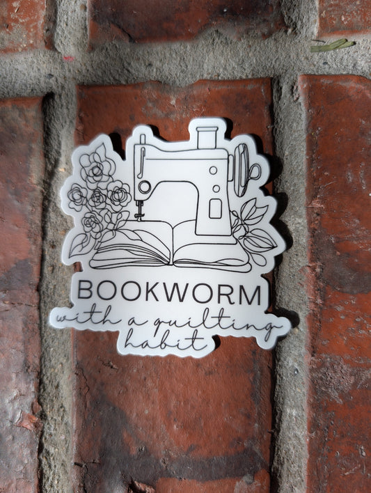 Sticker with sewing machine design and 'Bookworm with a quilt' text on a brick wall.